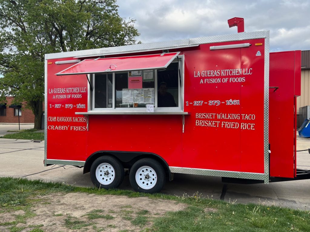 A red trailer called La Gueras Kitchen parked outside of a brewery offering dinner.