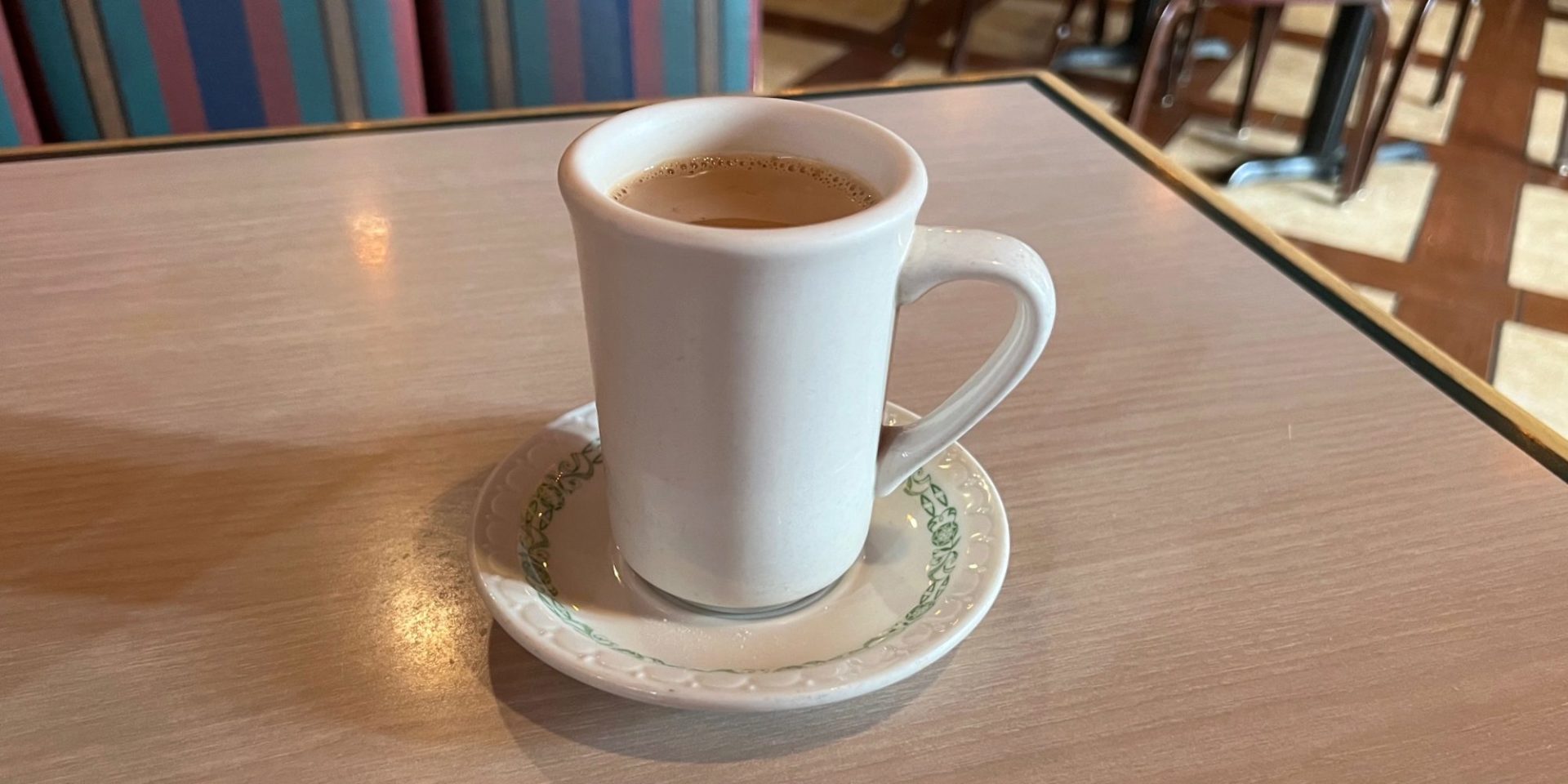 A white mug of masala tea on a table inside Kohinoor restaurant.