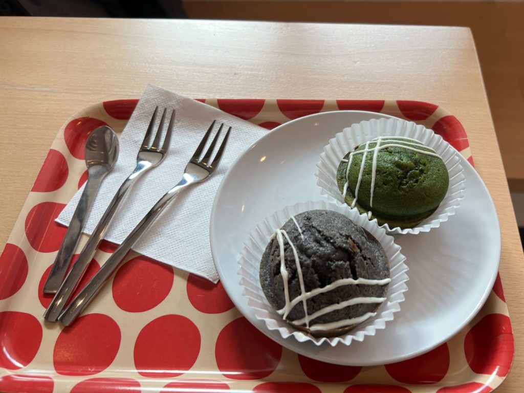 Two mochi cakes drizzled with white chocolate on a white plate on a tray tray with two metal forks and a spoon.