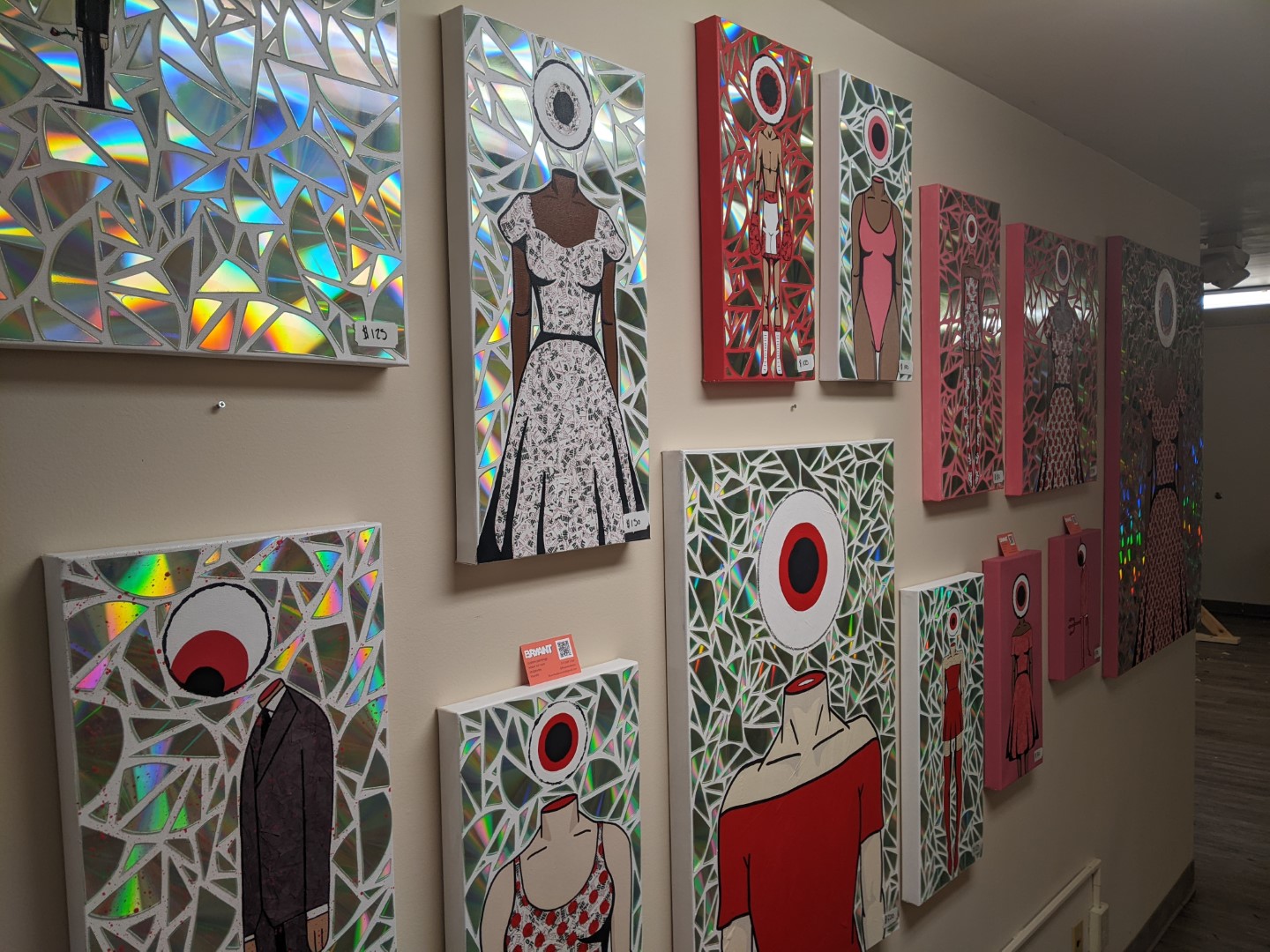 An art display of bodies with eyeballs for heads. They are painted and the background is small geometric shapes in holographic paper.