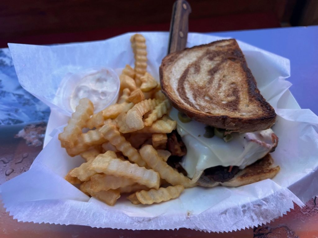 A patty melt served with a side of fries and a knife in a parchment paper lined basket.