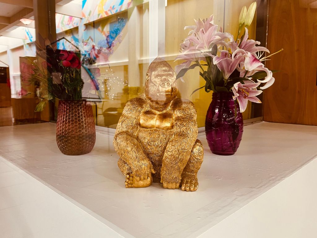 A window display in Lincoln Square Mall. A gold gorilla sits on a white shelf with two small vases of flowers.