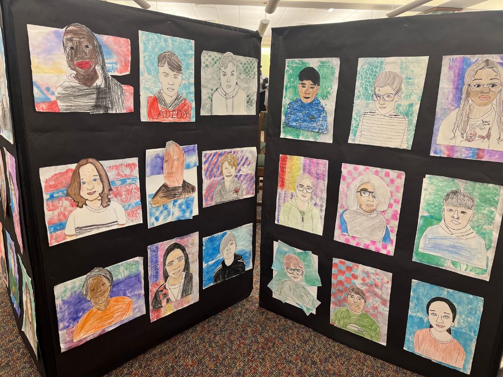 A display of colorful self portraits done by middle grade children. The portraits are colorful and laid out in a 3x3 grid.