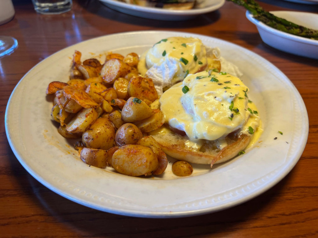 A side of fingerling potatoes with eggs benedict on a white plate.