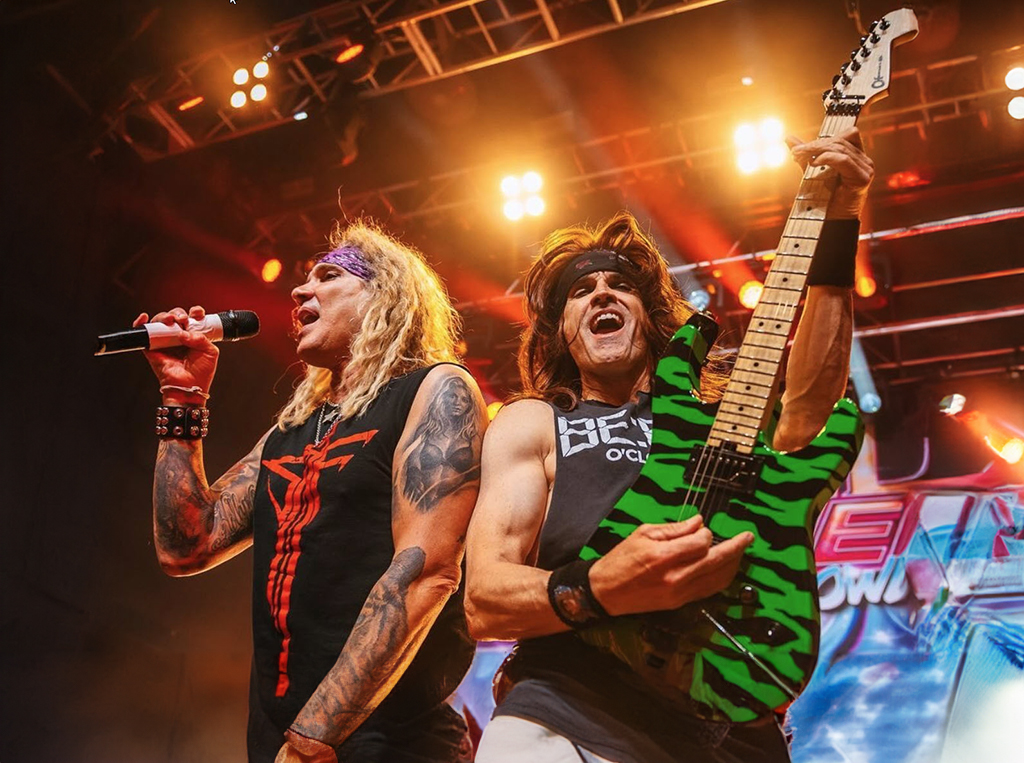 A glam rock singer and glam rock guitarist performing flamboyantly onstage.