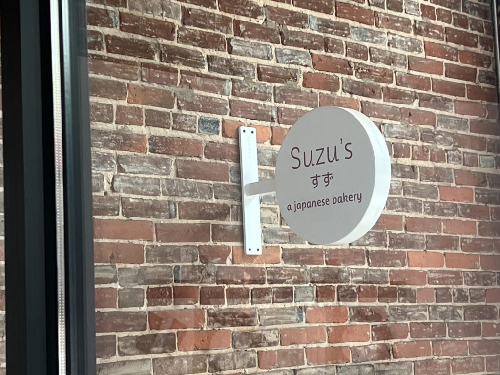 A brick exterior with a white circular sign reading "Suzu's a Japanese bakery"
