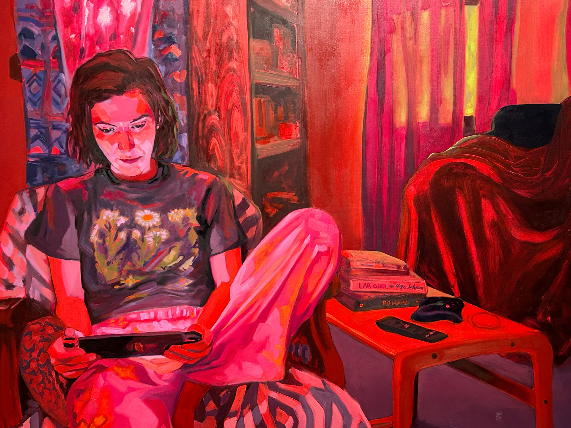 Painting of a person with brown hair playing a hand-held game. The painting is bright pink and blue. The woman sits on a chair by a table holding books and a television remote.