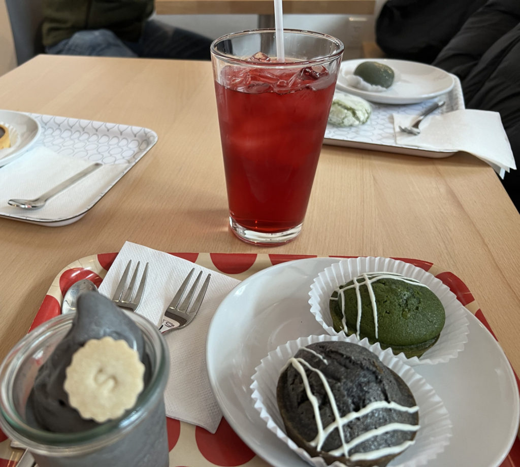 A glass cup of hibiscus pineapple tea beside a red tray of mochi treats and sesame soft serve.
