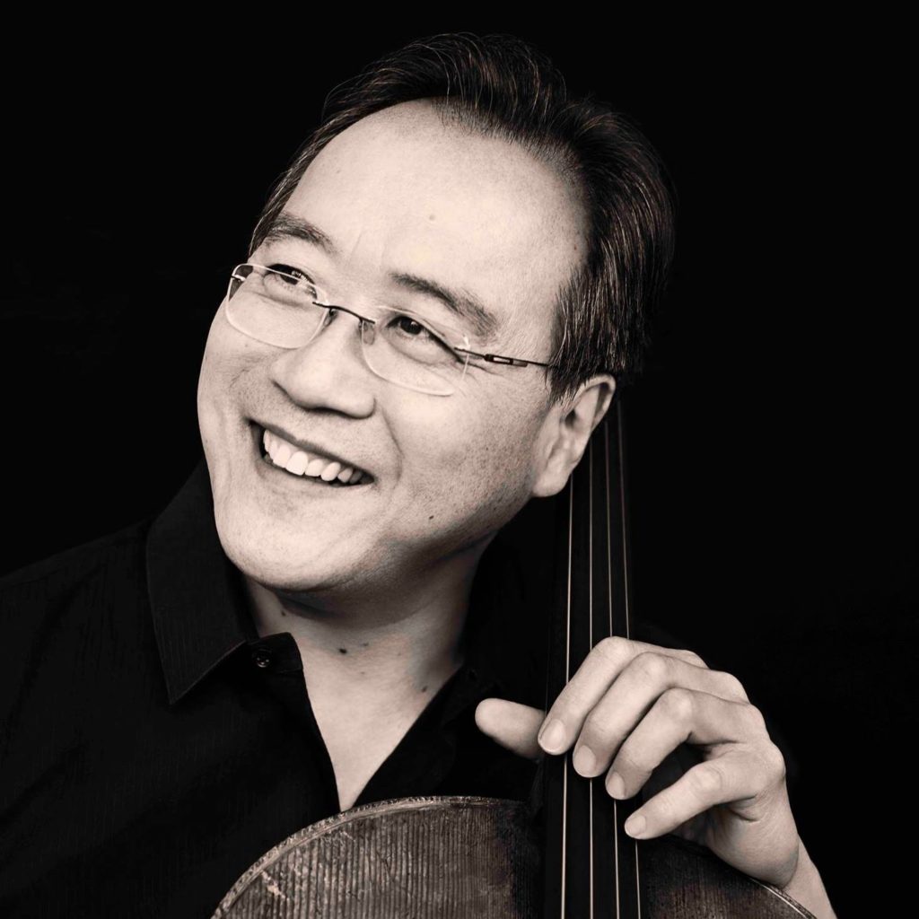 A black and white photo of Yo-Yo Ma, an man with Asian features. He is smiling and looking up to the left as he holds a cello.