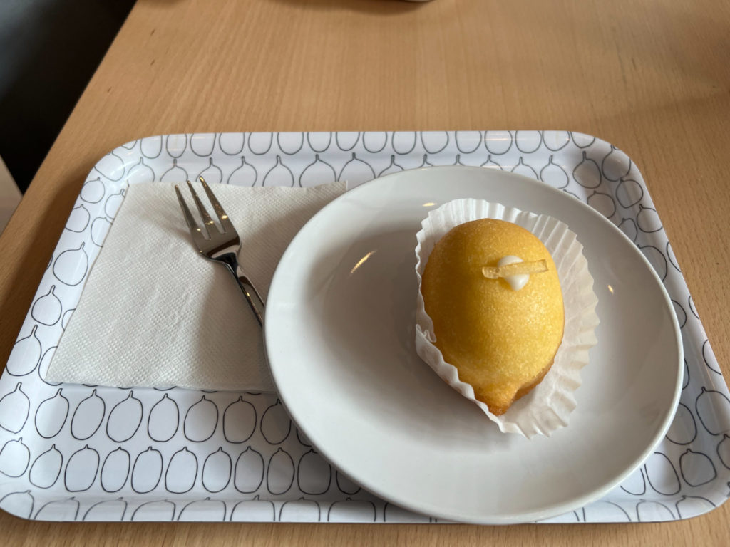 A yuzu cake on a white plate beside a metal fork on a white napkin.