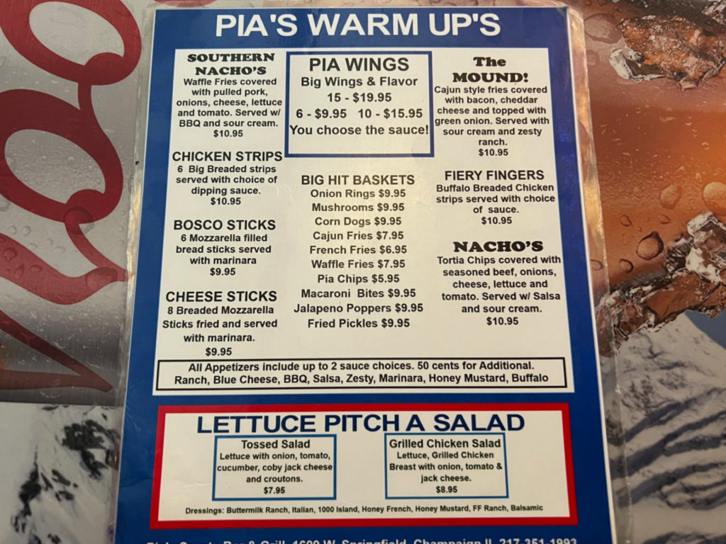A laminated menu for Pia's Warm-Ups (appetizers) sits on a Coors branded table at Pia's Sports Bar & Grill in Champaign.