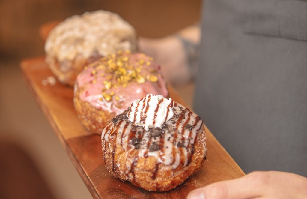 Three doughnuts on a wooden board held by white hands.