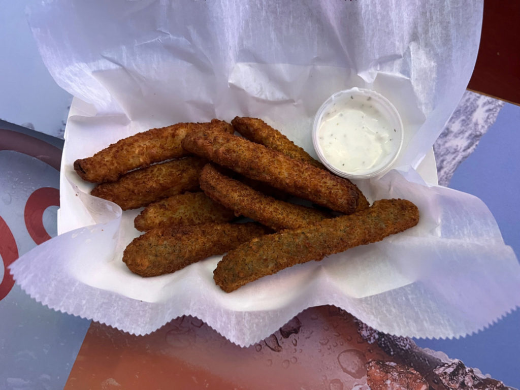 Fried pickles with a side of ranch dressing in a paper basket.