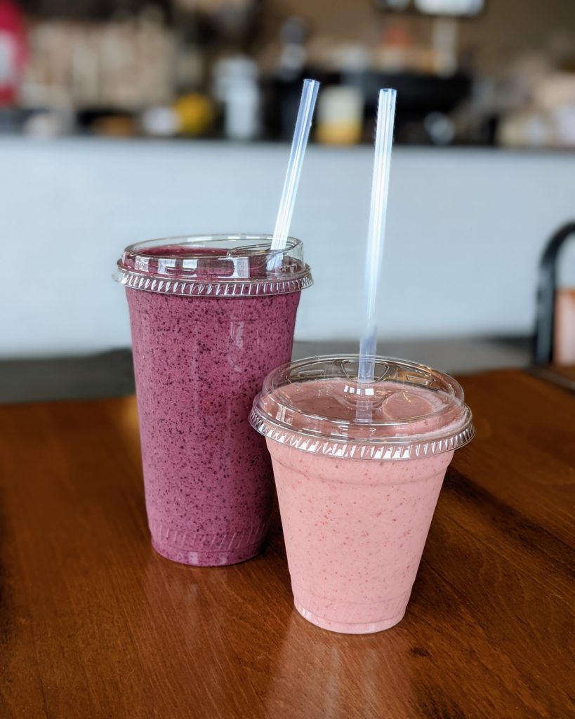 Two pink smoothies in clear plastic cups on a wooden table