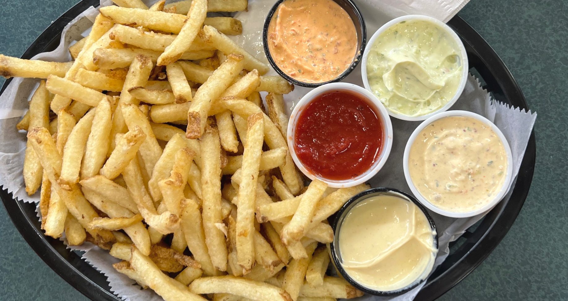 A black tray with fries and five sauces (orange, light green, deep red, yellow-orange, and yellow).