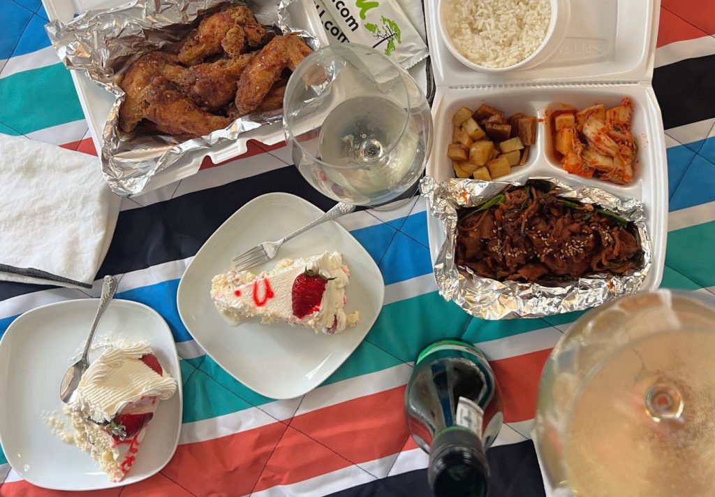 A picnic blanket of takeout Korean food and tres leches cake.