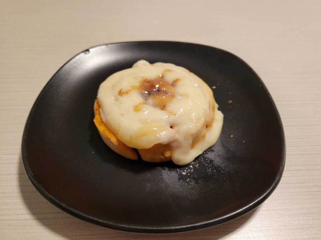 A warmed-up cinnamon roll on a small black plate.