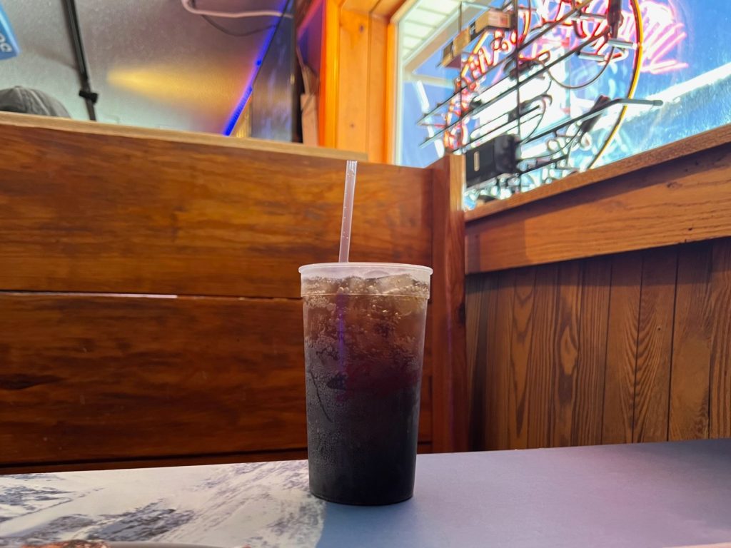 A cup of rum and coke is on a table in a wooden booth inside a sports bar in Champaign, Illinois.