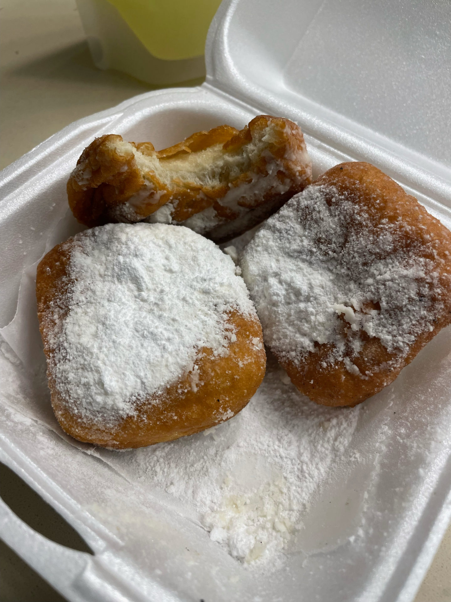 Three beignets in a white styrofoam box, and one of them has a bite out of it.