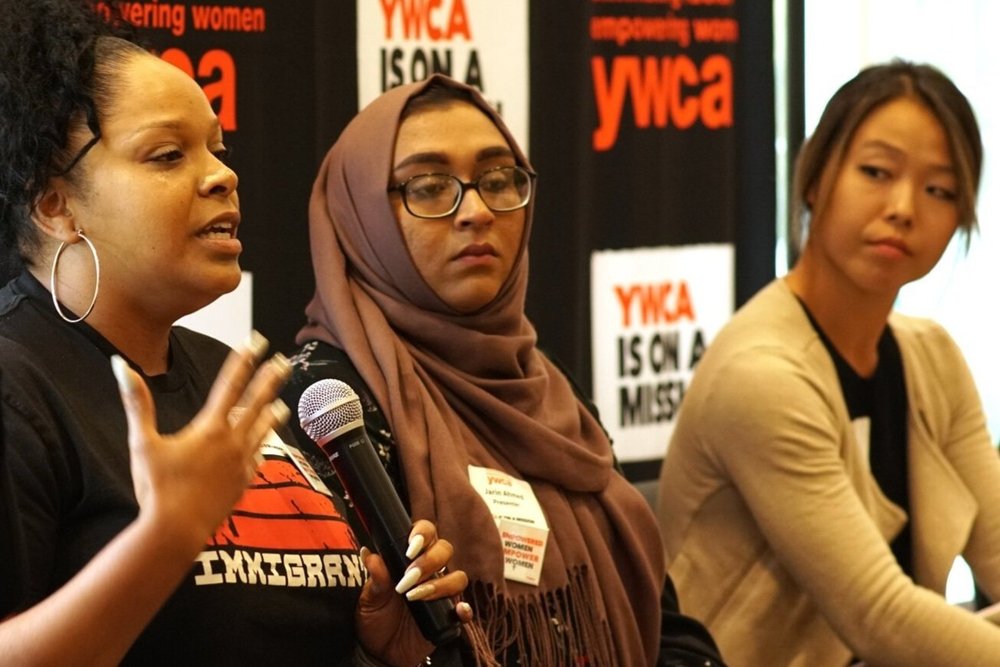 Three women sitting in a row, one Black woman speaking into a microphone on the far left