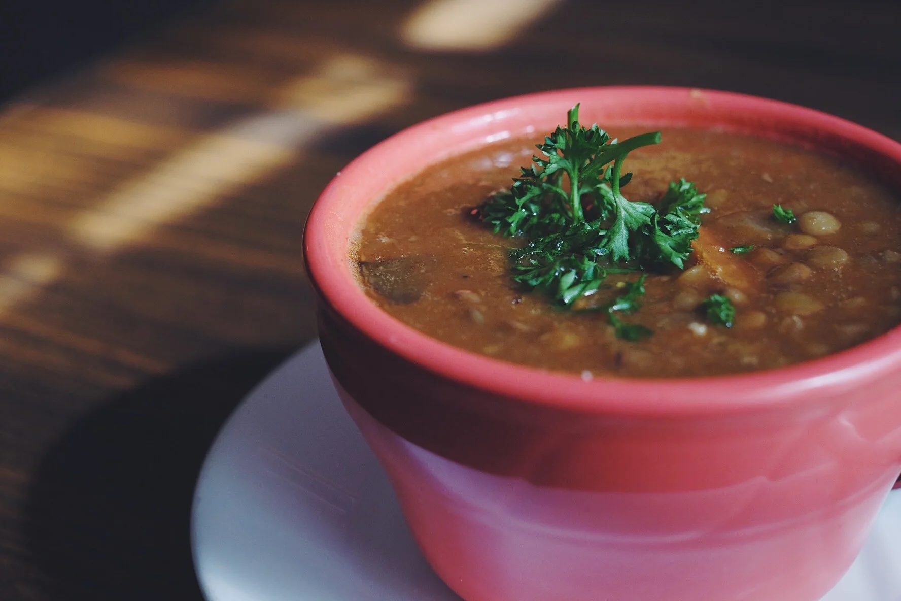 A red cup of brown soup with a green garnish on top
