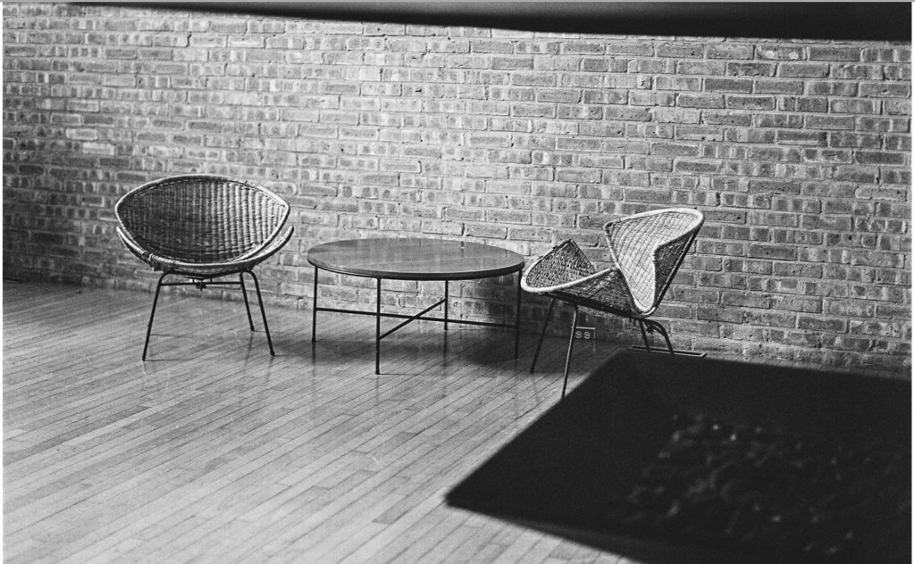 Black and white photo of two round wicker chairs and a round table against a brick wall.