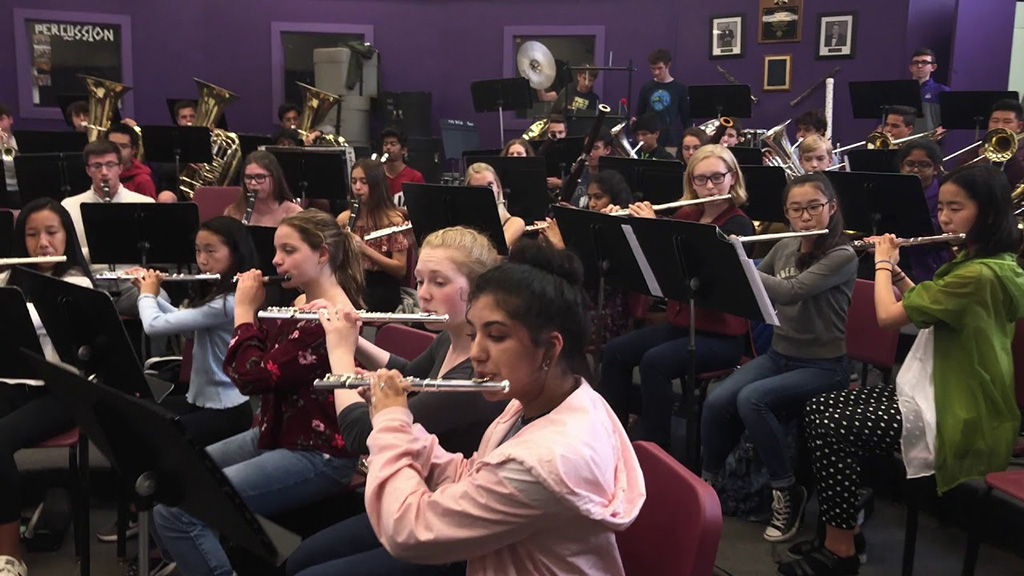 A high school concert band practicing. Students can be seen playing various instruments dressed casually implying that it's not an actual performance.