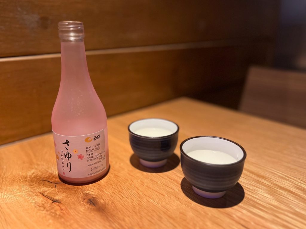 A bottle of pink sake beside two black handle-less teacups.