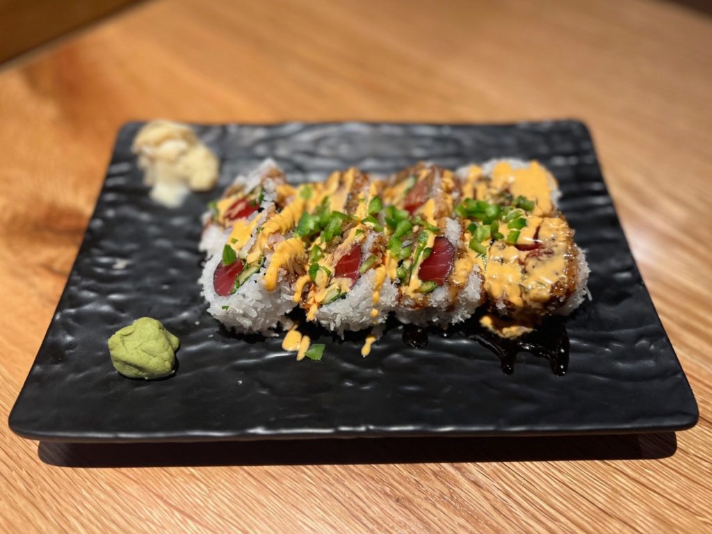A maki sushi roll with raw fatty tuna with a yellow sauce and raw jalapenos on a black plate.