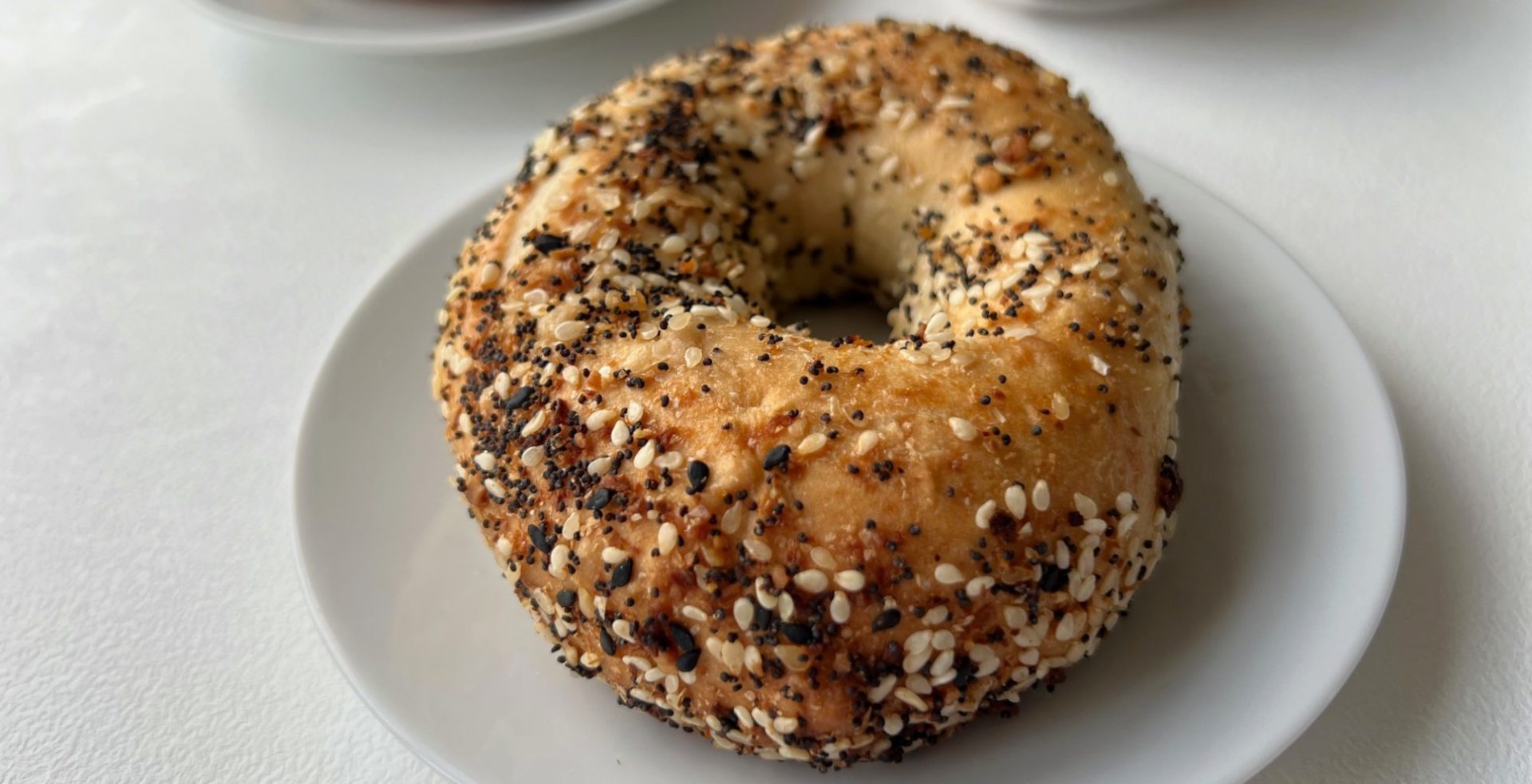 A bagel with everything seasoning on the outside on a white plate on a white table.