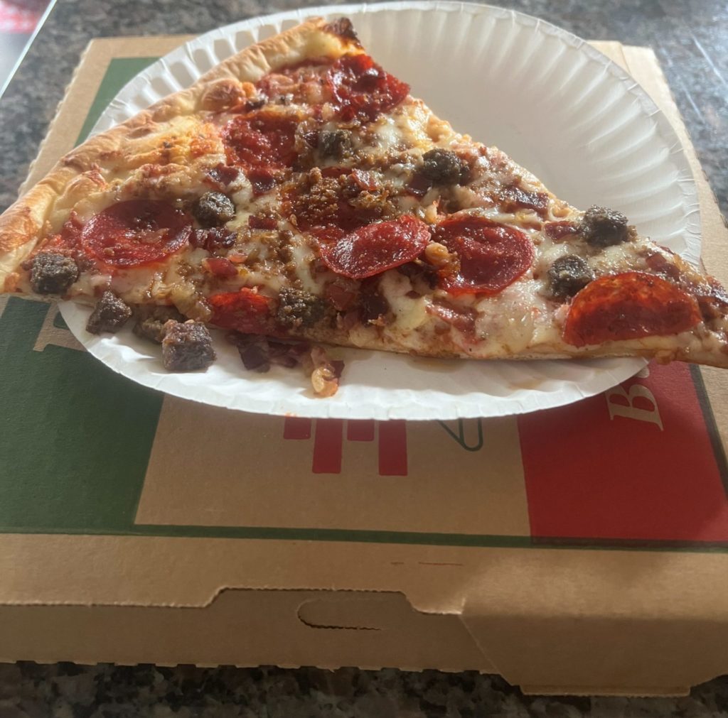 A single slice of pizza on a white paper plate on top of a brown pizza box.