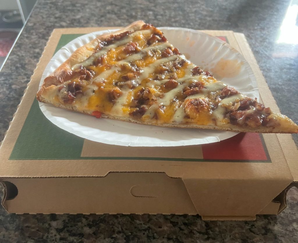 A slice of chicken bacon ranch on a white paper plate on a brown pizza box.