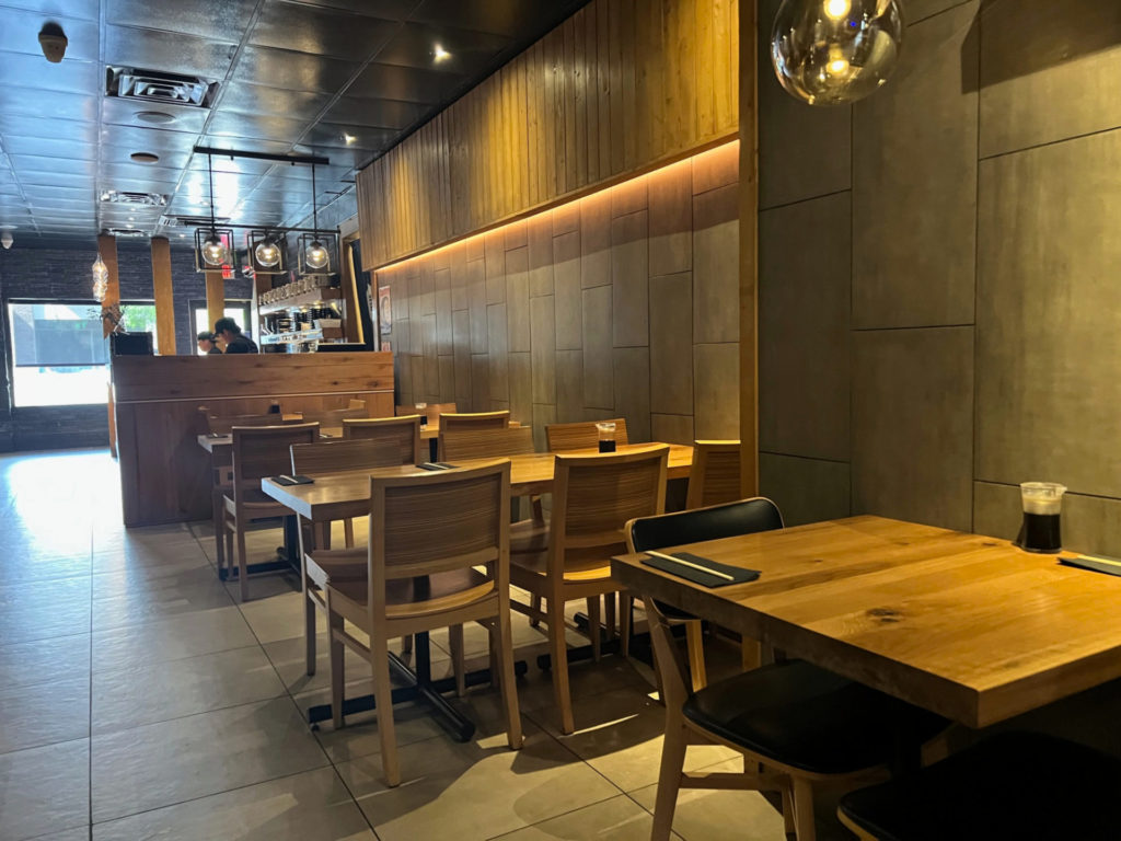 The interior of Sakanaya restaurant has four empty tables before a dinner rush with spherical lighting above a table for two and the sushi bar.