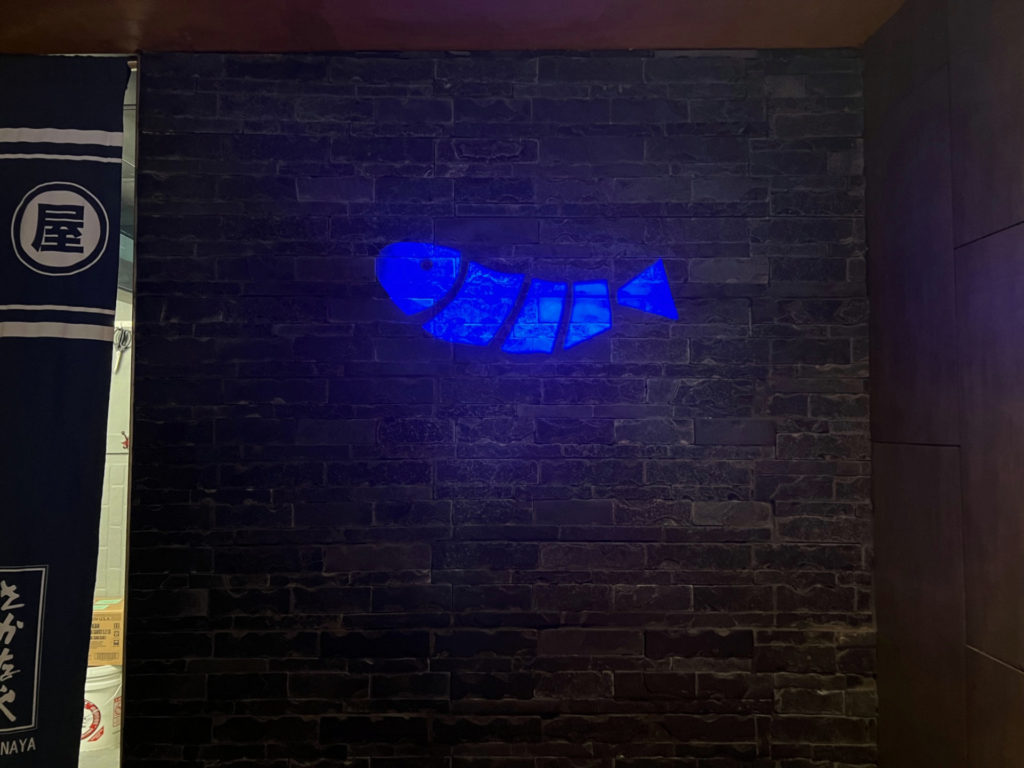 A black brick wall has an illuminated blue fish.