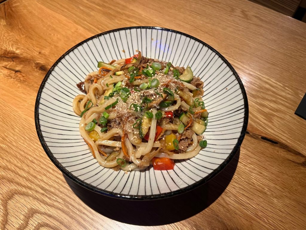 A bowl of beef yaki udon noodles in a white and black bowl.