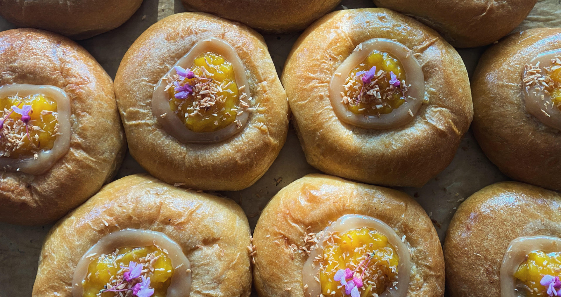 Several round pastries have a light orange center with a bright orange jam and edible flowers.